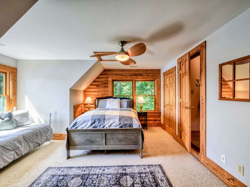 A bright and airy bedroom features a comfortable queen bed, a daybed with picturesque lake views, rustic accents, and an en suite bathroom for convenience.
