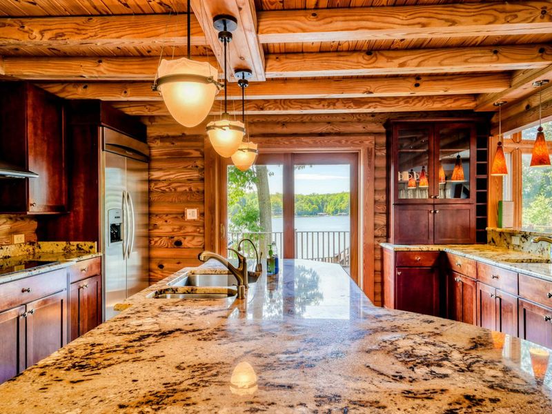 A spacious kitchen with granite countertops and wood cabinetry opens to a deck with stunning lake views.