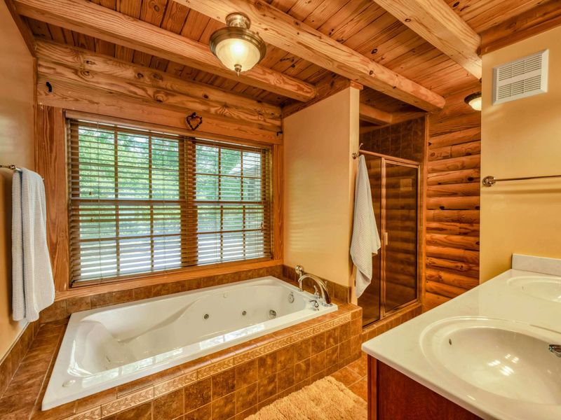 A luxurious en suite bathroom features a jetted soaking tub, a spacious walk-in shower, double sinks with a large vanity, and warm wood accents for a cozy yet elegant retreat.