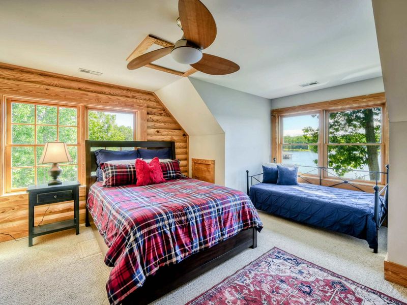 A charming bedroom with a queen bed, a daybed, and large windows offering stunning lake views, complemented by an en suite bathroom for added convenience.