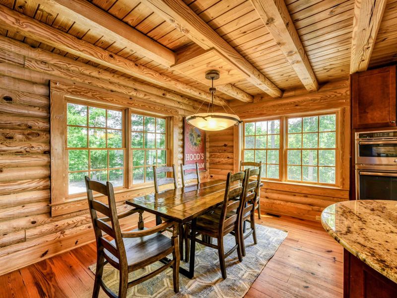 A cozy dining nook with a wooden table, surrounded by large windows that bring in natural light and views of the surrounding greenery.