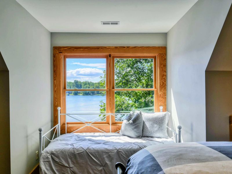 A bright and airy bedroom features a comfortable queen bed, a daybed with picturesque lake views, rustic accents, and an en suite bathroom for convenience.