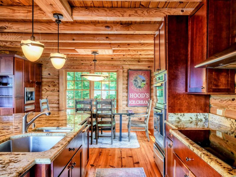 A beautifully designed kitchen with granite countertops, rich wood cabinets, and a cozy dining area framed by large windows and rustic decor.