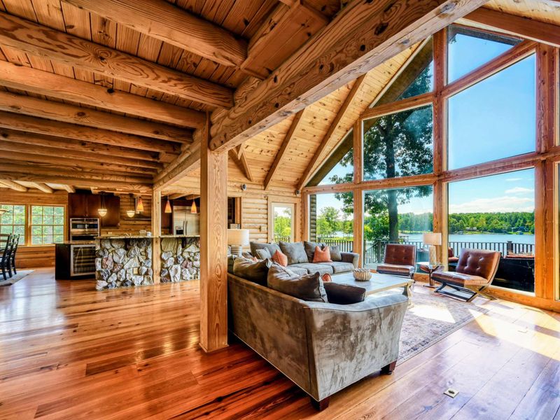A warm and inviting open-concept living space features plush seating, vaulted wooden ceilings, and large windows with stunning lake views.