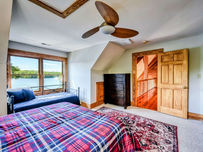 A charming bedroom with a queen bed, a daybed, and large windows offering stunning lake views, complemented by an en suite bathroom for added convenience.