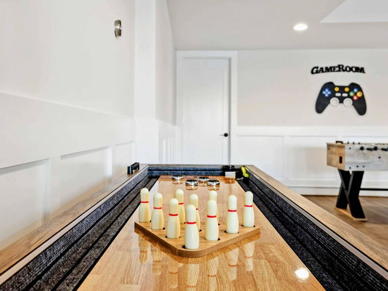 This spacious game room features a comfortable seating area with a modern fireplace, a pool table, ping-pong table, foosball table, shuffleboard, and a well-equipped kitchenette, all with stunning lake views.