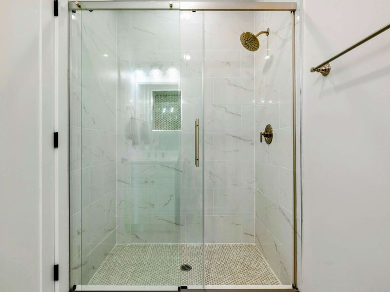 A modern en suite bathroom features a sleek glass shower, single vanity, and fresh accents that connect seamlessly to the adjoining bedroom.