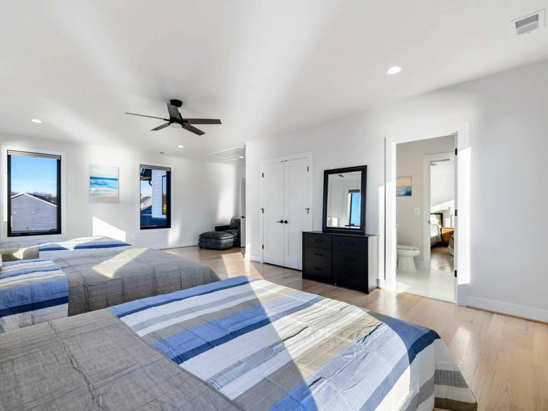 A spacious, well-lit bedroom with large windows offering stunning lake views, featuring three comfortable queen beds, modern furnishings, and a convenient Jack and Jill bathroom for shared access.