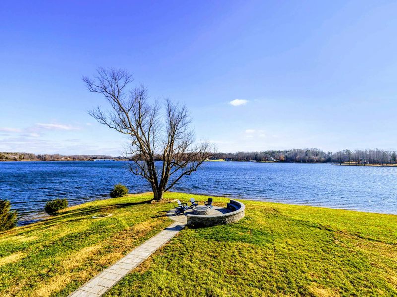 Fire Pit - Gas fire pit nested in pavers at the water's edge, ring of Adirondacks under a single tree, lake on three sides.