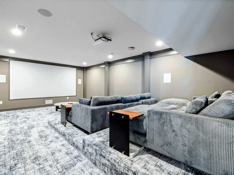 A dedicated home theater with tiered seating, plush couches, a large projector screen, and cozy cinema-themed decor for an immersive movie experience.