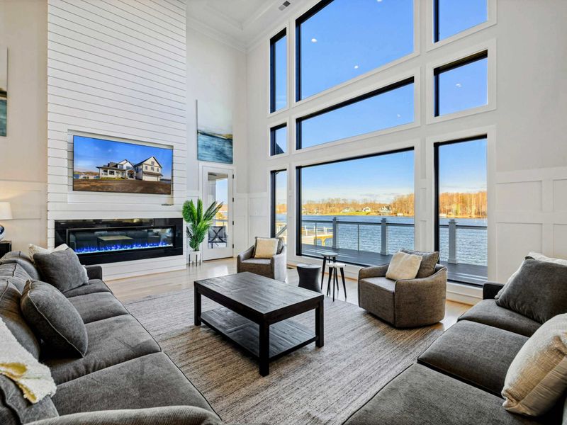 Great Room - Two-story windows, a long fireplace, and the dock visible just past the rail. The room everyone gathers in.