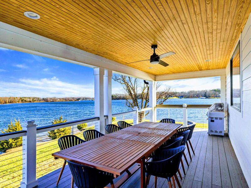 An expansive lakeside deck featuring stunning water views, comfortable seating, and a spacious dining area perfect for outdoor relaxation or entertaining.
