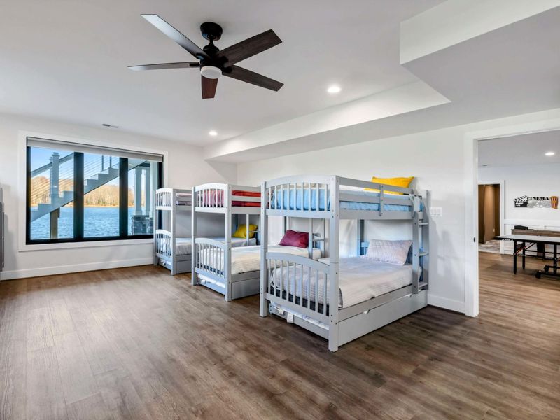 A spacious bunk room featuring 12 twin beds, modern decor, large windows with lake views, and an ensuite bathroom for group convenience.