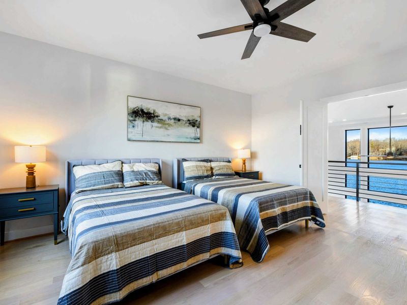 A serene bedroom featuring two cozy queen beds, modern decor, a large window with stunning lake views, and access to a convenient Jack and Jill bathroom.