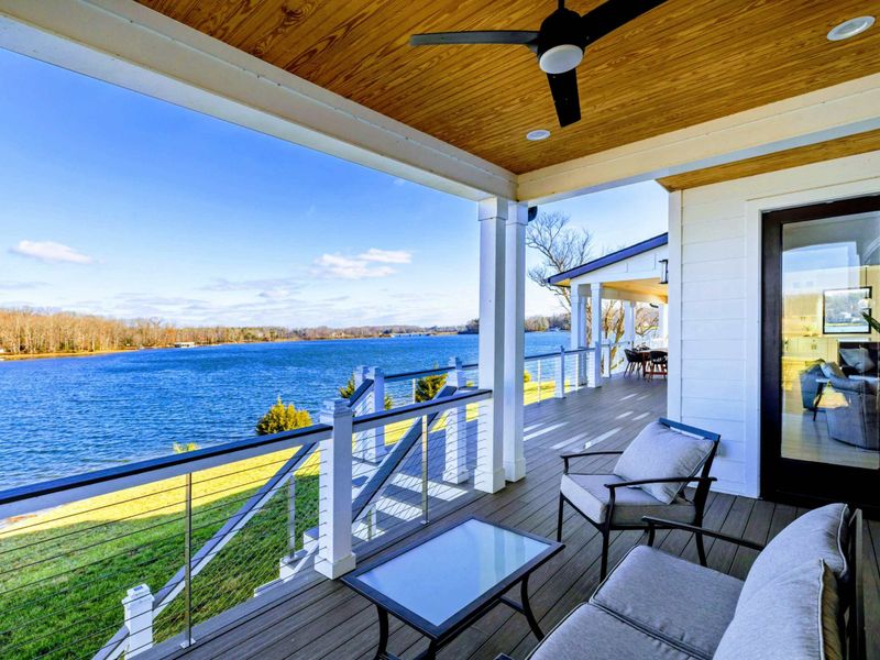 An expansive lakeside deck featuring stunning water views, comfortable seating, and a spacious dining area perfect for outdoor relaxation or entertaining.