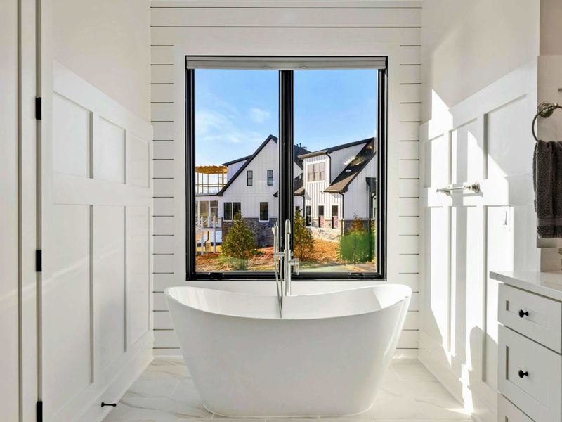 A luxurious en suite bathroom featuring dual vanities, a freestanding soaking tub with scenic views, and a spacious glass-enclosed shower with elegant tile and gold fixtures.