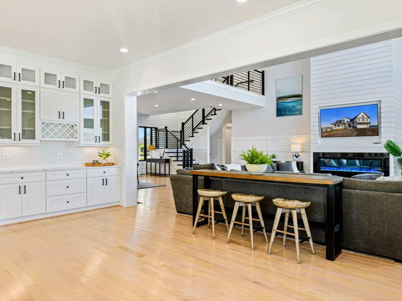 This modern and spacious kitchen features a large island with bar seating, elegant cabinetry, high-end appliances, and expansive windows showcasing scenic lake views, seamlessly flowing into the open concept living room.