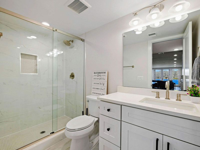 Full Bath - Glass-enclosed shower with marble tile, single vanity. Serves the lake-level bunk and game spaces.