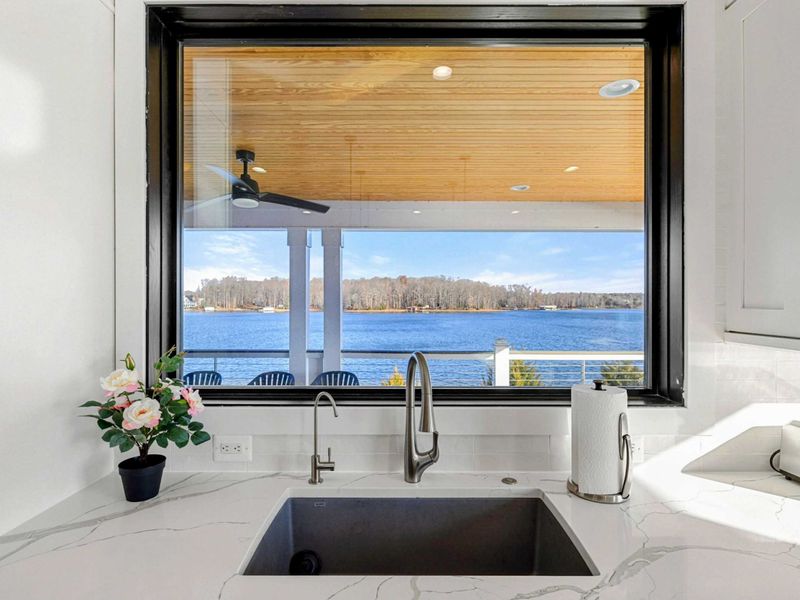 This modern and spacious kitchen features a large island with bar seating, elegant cabinetry, high-end appliances, and expansive windows showcasing scenic lake views, seamlessly flowing into the open concept living room.