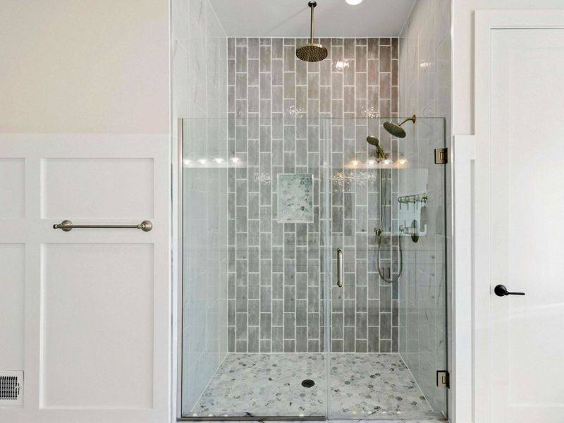 A luxurious en suite bathroom featuring dual vanities, a freestanding soaking tub with scenic views, and a spacious glass-enclosed shower with elegant tile and gold fixtures.