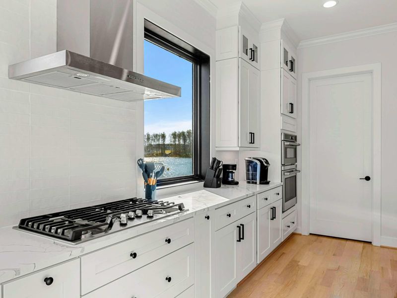 This modern and spacious kitchen features a large island with bar seating, elegant cabinetry, high-end appliances, and expansive windows showcasing scenic lake views, seamlessly flowing into the open concept living room.