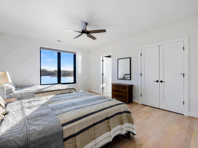 A serene bedroom featuring two cozy queen beds, modern decor, a large window with stunning lake views, and access to a convenient Jack and Jill bathroom.