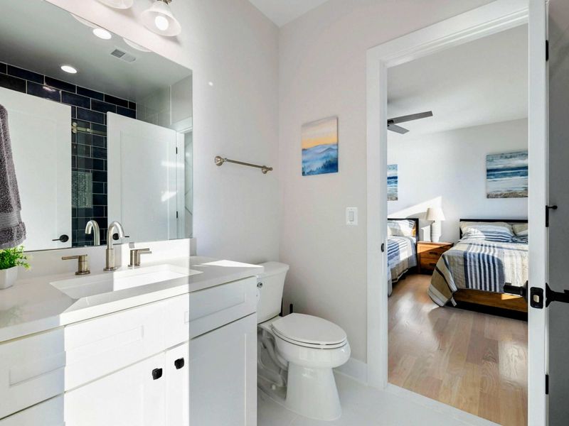 A modern Jack and Jill bathroom featuring sleek black tile accents, a spacious glass-enclosed shower, double vanity, and direct access to adjoining bedrooms.