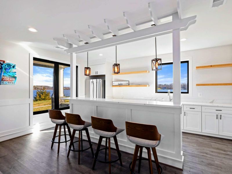 This spacious game room features a comfortable seating area with a modern fireplace, a pool table, ping-pong table, foosball table, shuffleboard, and a well-equipped kitchenette, all with stunning lake views.