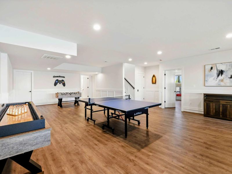 This spacious game room features a comfortable seating area with a modern fireplace, a pool table, ping-pong table, foosball table, shuffleboard, and a well-equipped kitchenette, all with stunning lake views.