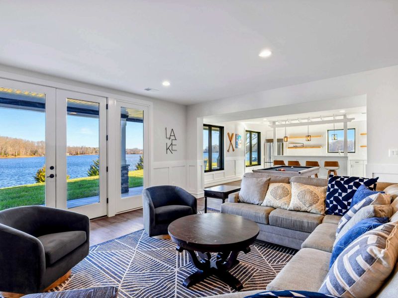 This spacious game room features a comfortable seating area with a modern fireplace, a pool table, ping-pong table, foosball table, shuffleboard, and a well-equipped kitchenette, all with stunning lake views.