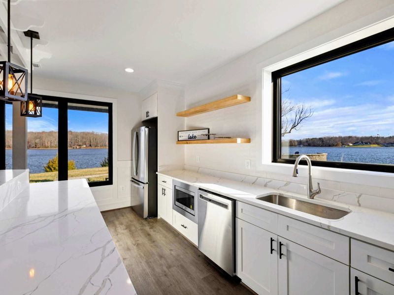 This spacious game room features a comfortable seating area with a modern fireplace, a pool table, ping-pong table, foosball table, shuffleboard, and a well-equipped kitchenette, all with stunning lake views.