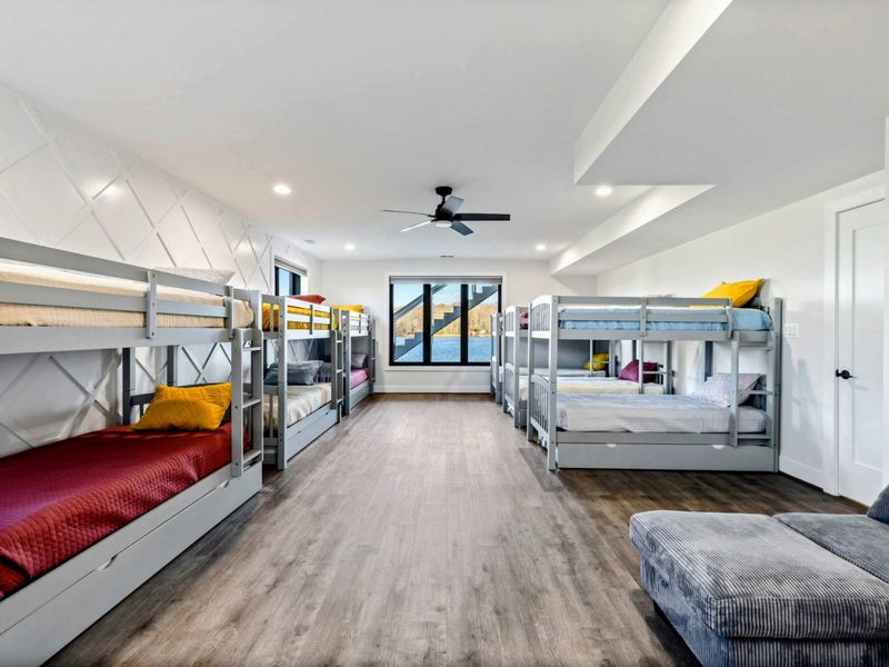 A spacious bunk room featuring 12 twin beds, modern decor, large windows with lake views, and an ensuite bathroom for group convenience.