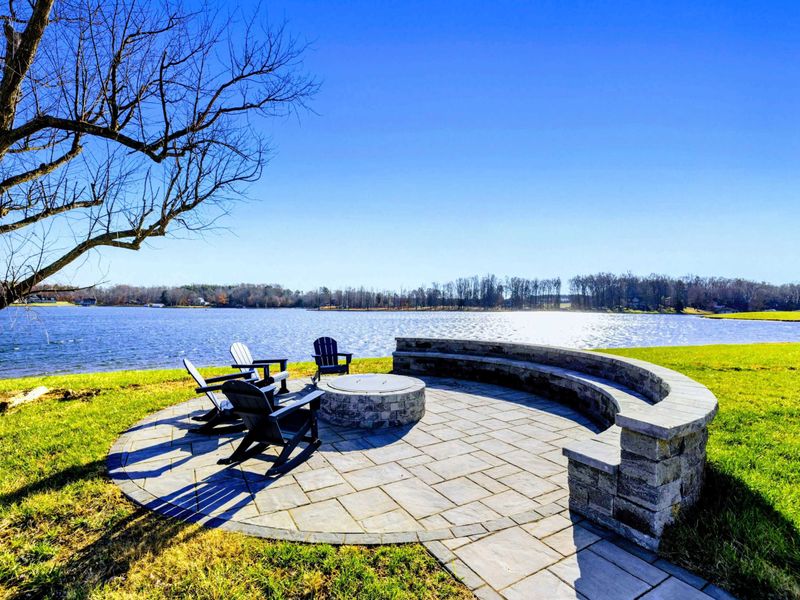 A scenic lakeside fire pit area with Adirondack chairs and a paved patio, offering a perfect spot to relax and enjoy the water views.