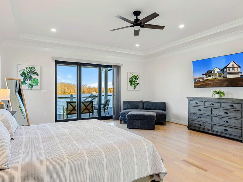 This spacious primary bedroom features a comfortable bed, a private seating area, access to a balcony with stunning lake views, and an en suite bathroom for added convenience.