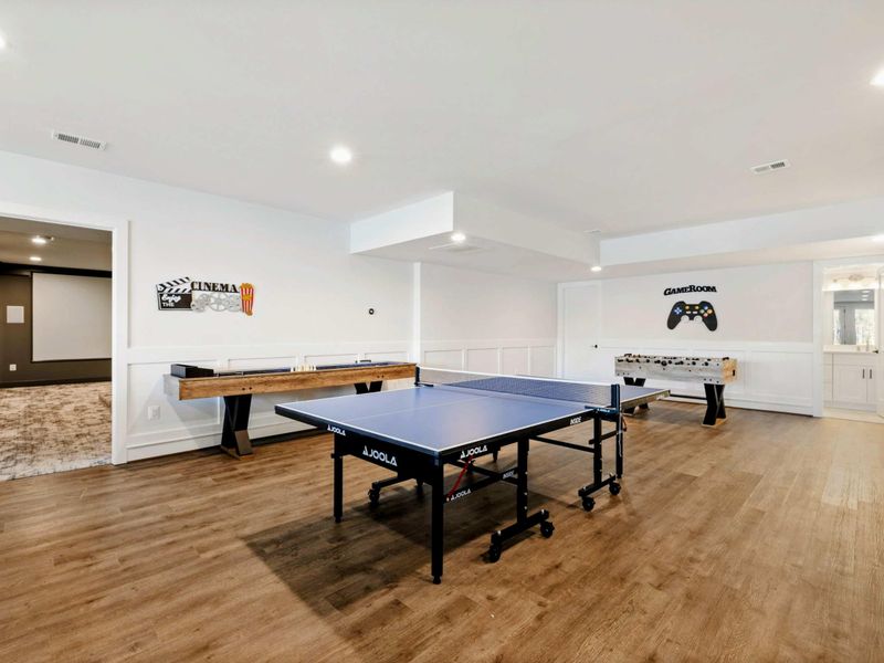 This spacious game room features a comfortable seating area with a modern fireplace, a pool table, ping-pong table, foosball table, shuffleboard, and a well-equipped kitchenette, all with stunning lake views.