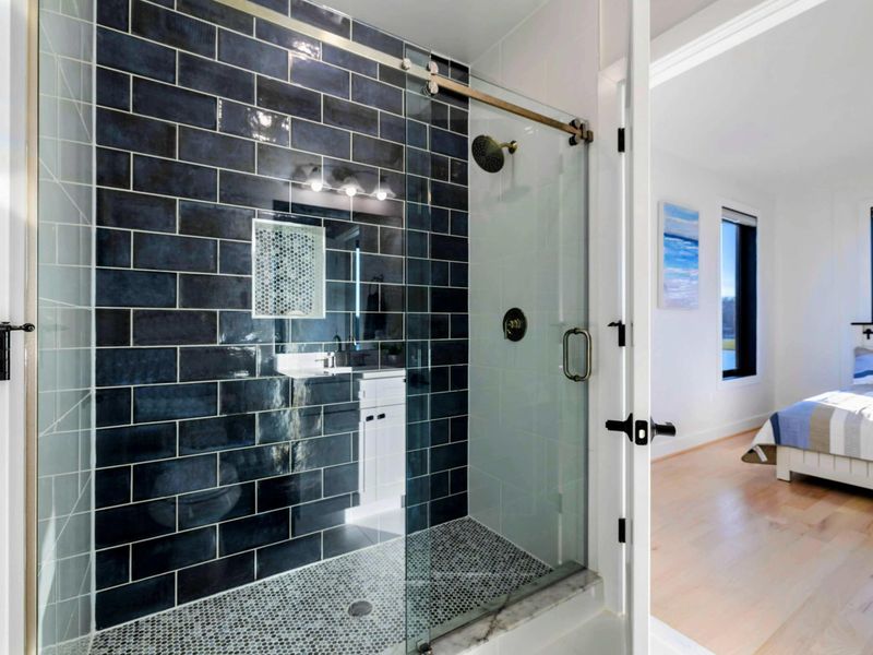 Full Bath - Glass-enclosed shower with deep-blue subway tile and brushed-brass fixtures. Shared between the upstairs suites.