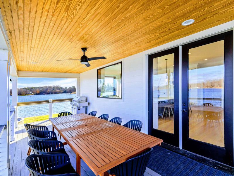 An expansive lakeside deck featuring stunning water views, comfortable seating, and a spacious dining area perfect for outdoor relaxation or entertaining.
