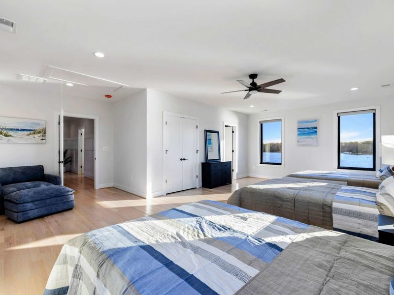A spacious, well-lit bedroom with large windows offering stunning lake views, featuring three comfortable queen beds, modern furnishings, and a convenient Jack and Jill bathroom for shared access.