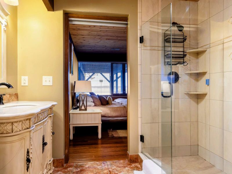 This en-suite bathroom connects to the bedroom, featuring a glass-enclosed shower, decorative vanity, and warm tones for a cohesive and inviting design.