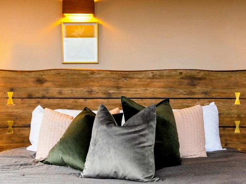 The centerpiece of this room is a stunning wooden bed frame featuring unique gold accents, complemented by plush pillows and cozy bedding for a luxurious touch.