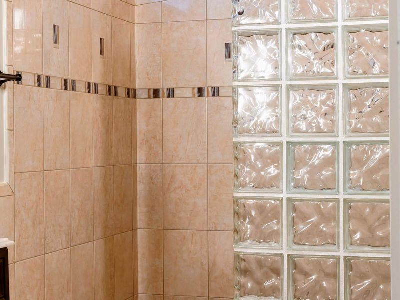 The walk-in shower in the primary suite bathroom features elegant tile work and a stylish glass block partition, offering a spacious and private bathing area.