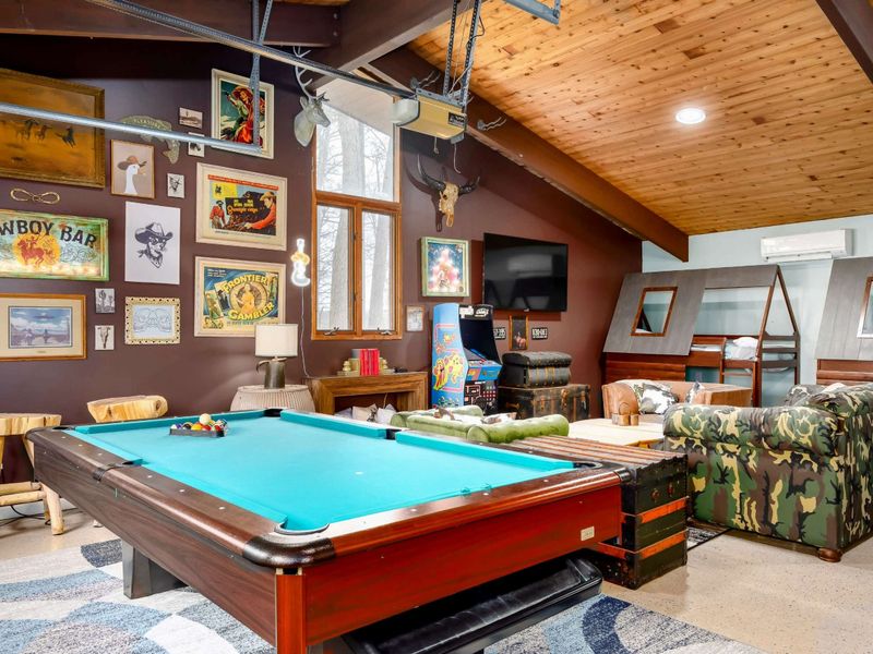 The Game Room offers a vibrant space filled with entertainment, including a pool table, retro arcade games, and unique cabin-style bunk beds, all set against a backdrop of eclectic western-inspired decor for an unforgettable experience.