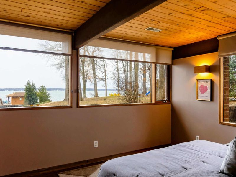 This bedroom boasts expansive windows, offering serene views of the lake and surrounding nature, creating a tranquil retreat.