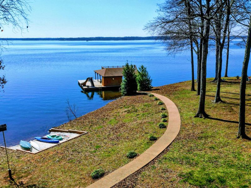 Scenic lakeside property with a winding path leading to a private boathouse and water slide, perfect for waterfront relaxation.