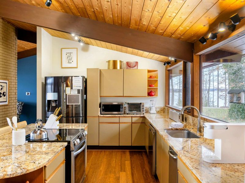 The kitchen combines functionality and elegance with its sleek cabinetry, granite countertops, and stainless steel appliances, all framed by stunning lake views through large windows.