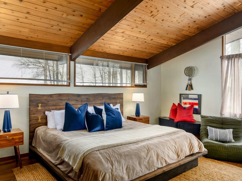 A cozy primary suite showcasing a rustic wooden bed, plush pillows, and bedside tables with elegant lamps. The seating area adds a touch of relaxation to this tranquil space.
