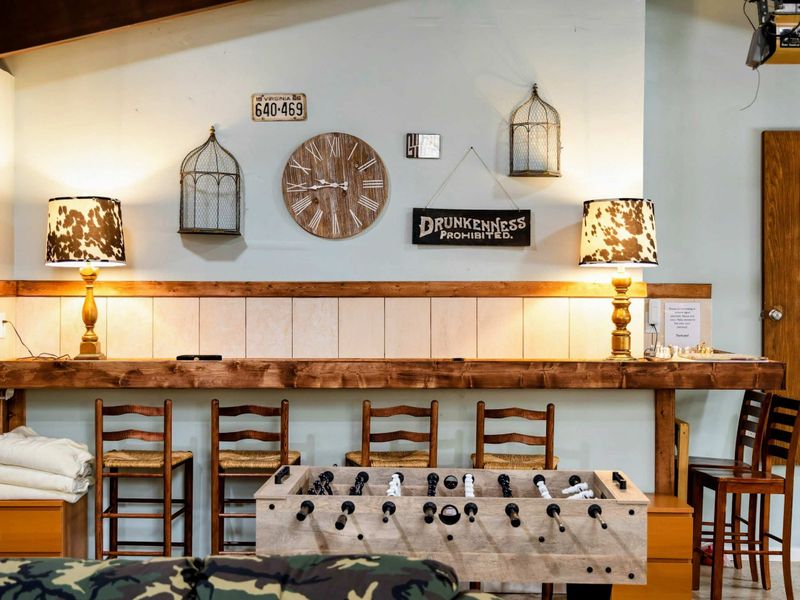 The Game Room's rustic charm is highlighted by a cozy bar with wooden stools, warm lighting, and quirky decor, creating an inviting space for relaxation and casual gatherings.
