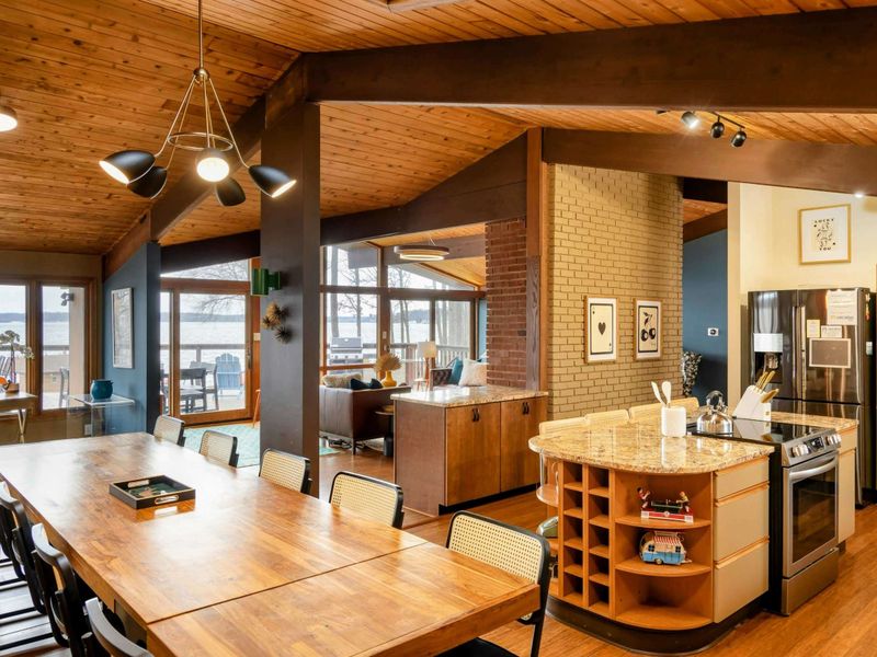 The open-concept dining and kitchen area features a large wooden table perfect for gatherings, seamlessly connecting to the gourmet kitchen with granite countertops and a view of the lake, creating a warm and inviting space for shared meals and conve
