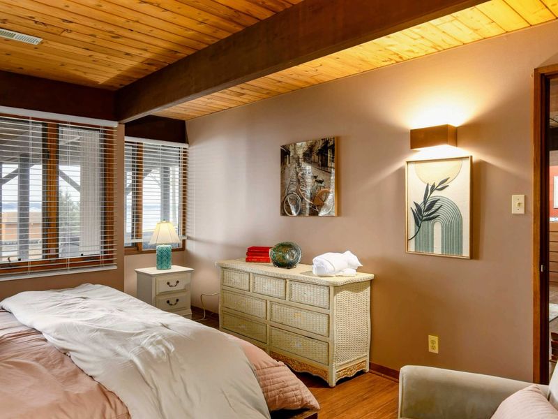 This serene bedroom features wicker furniture, warm lighting, and decor that adds charm and character. Large windows frame scenic views, enhancing the tranquil atmosphere.