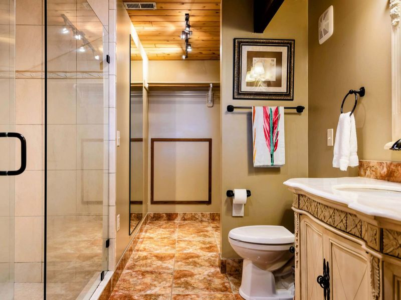 This bathroom boasts a spacious glass-enclosed shower, elegant vanity with intricate details, and warm lighting, creating a functional yet inviting space.